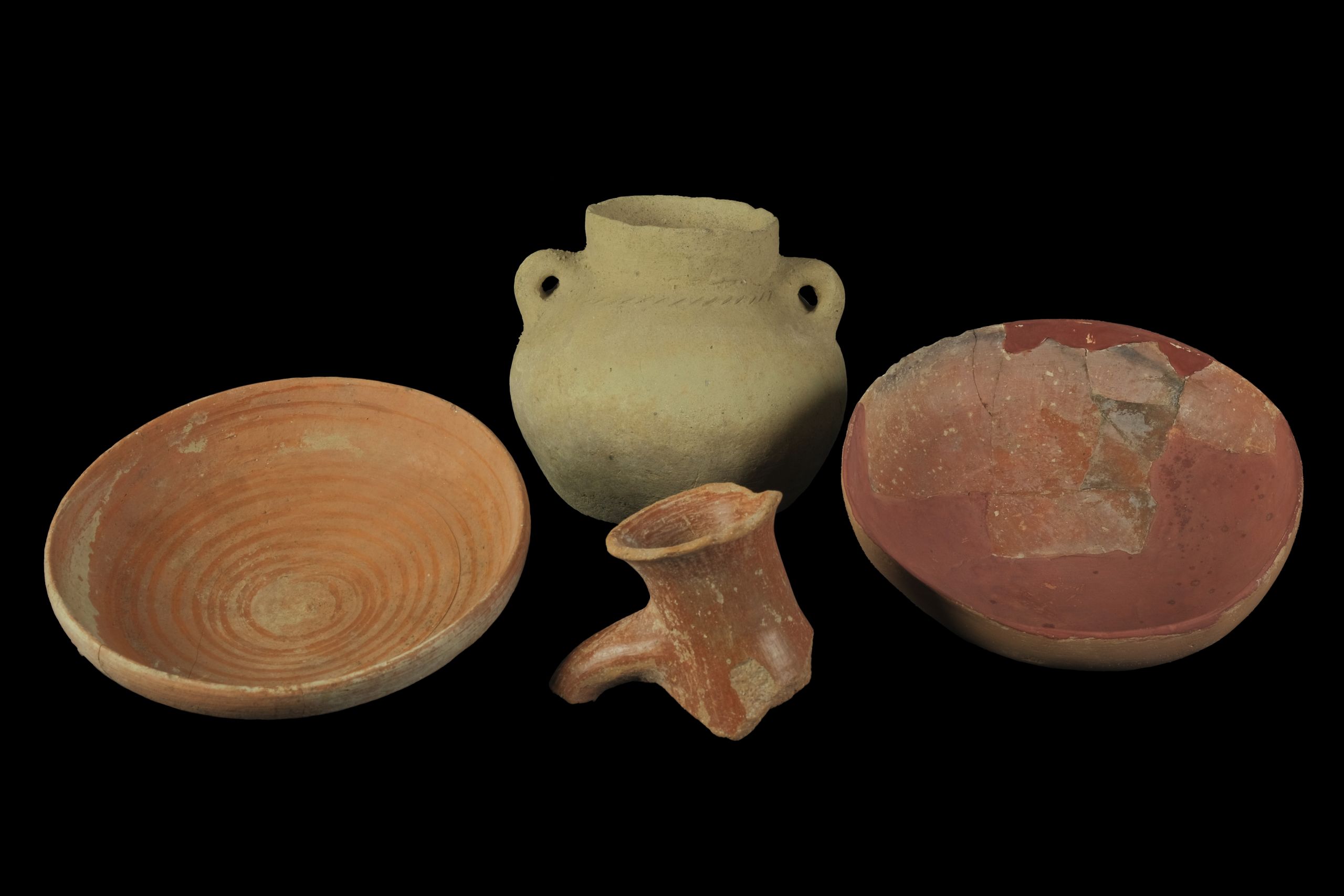 A shallow reddish bowl, a jug decorated with diagonal slashes, a bowl reconstructed with red plaster, and the rim and neck fragment of a jug