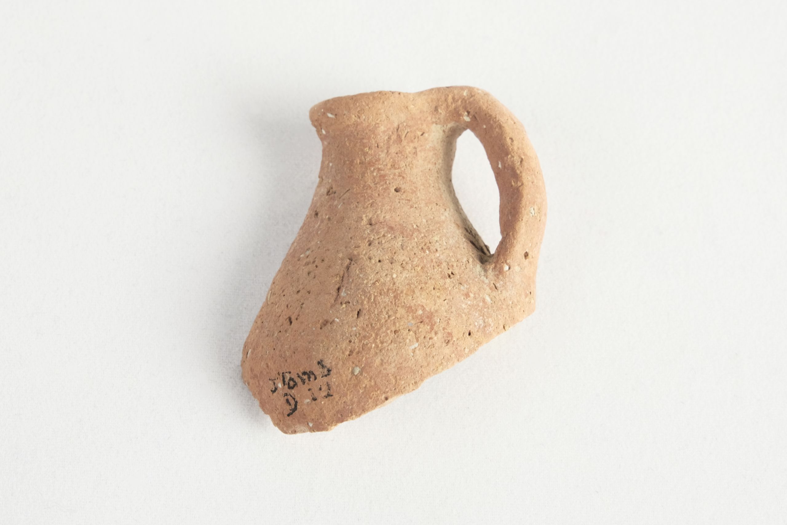 Broken sherd of a small orange jug with a handle attached