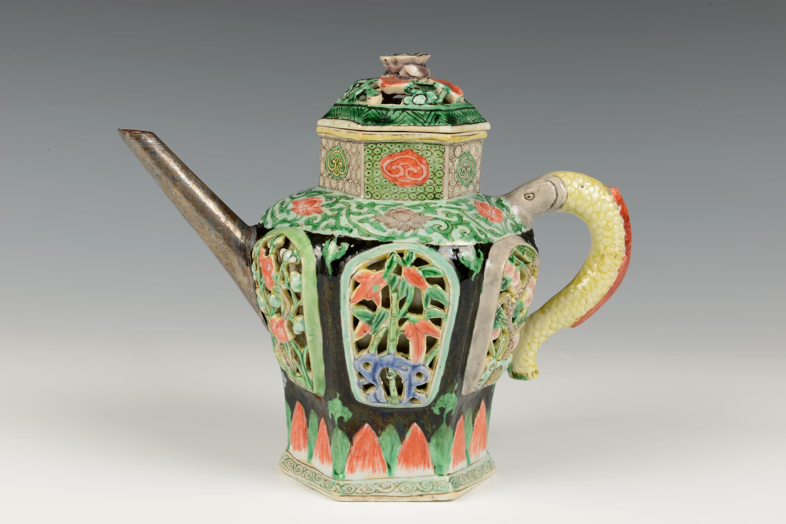 Intricately decorated teapot with green, red and black patterns and a long golden spout.