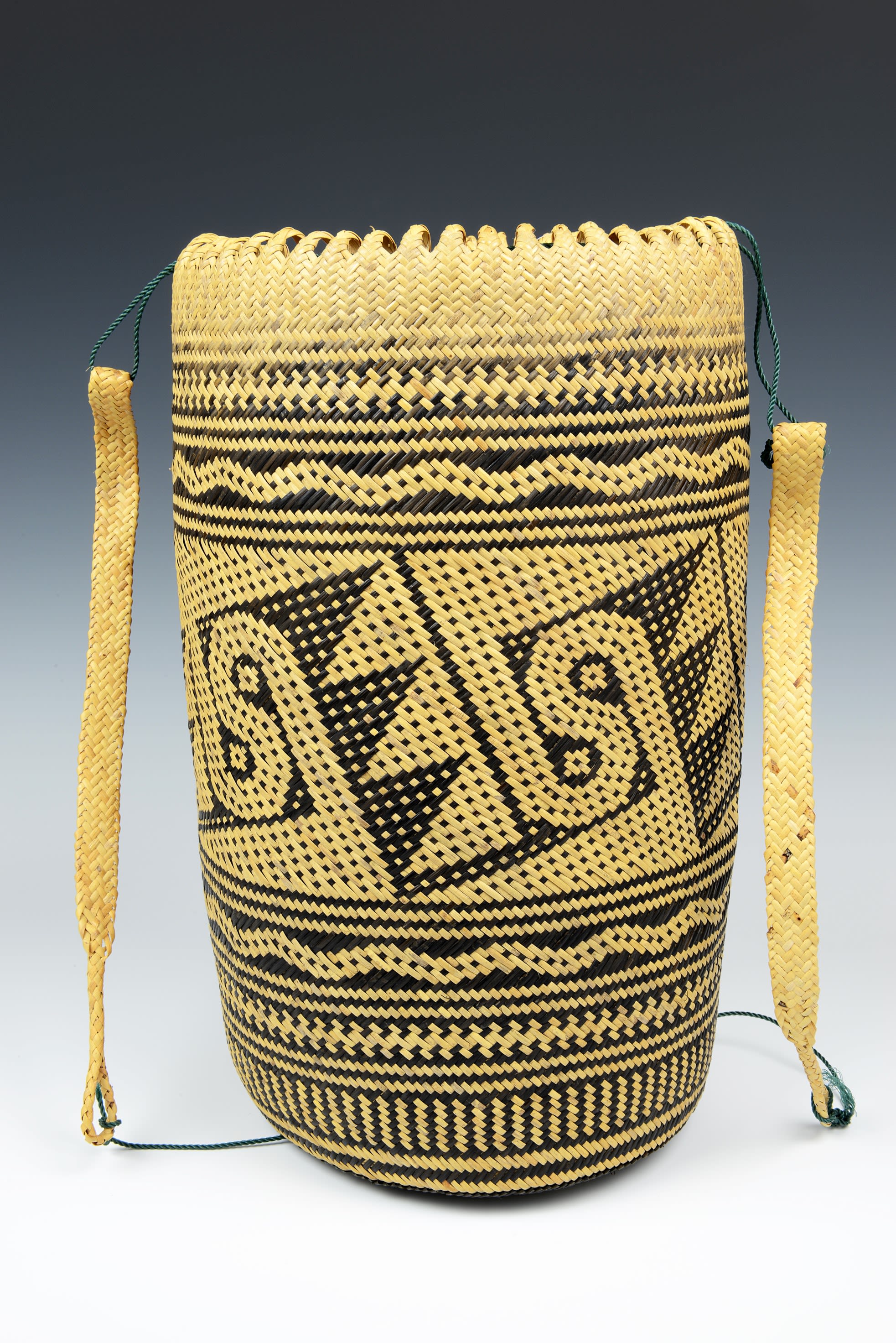 Woven basket coloured yellow and black. The patterned design consists of triangles, waves and curves. The basket has two carrying handles draped at either side.