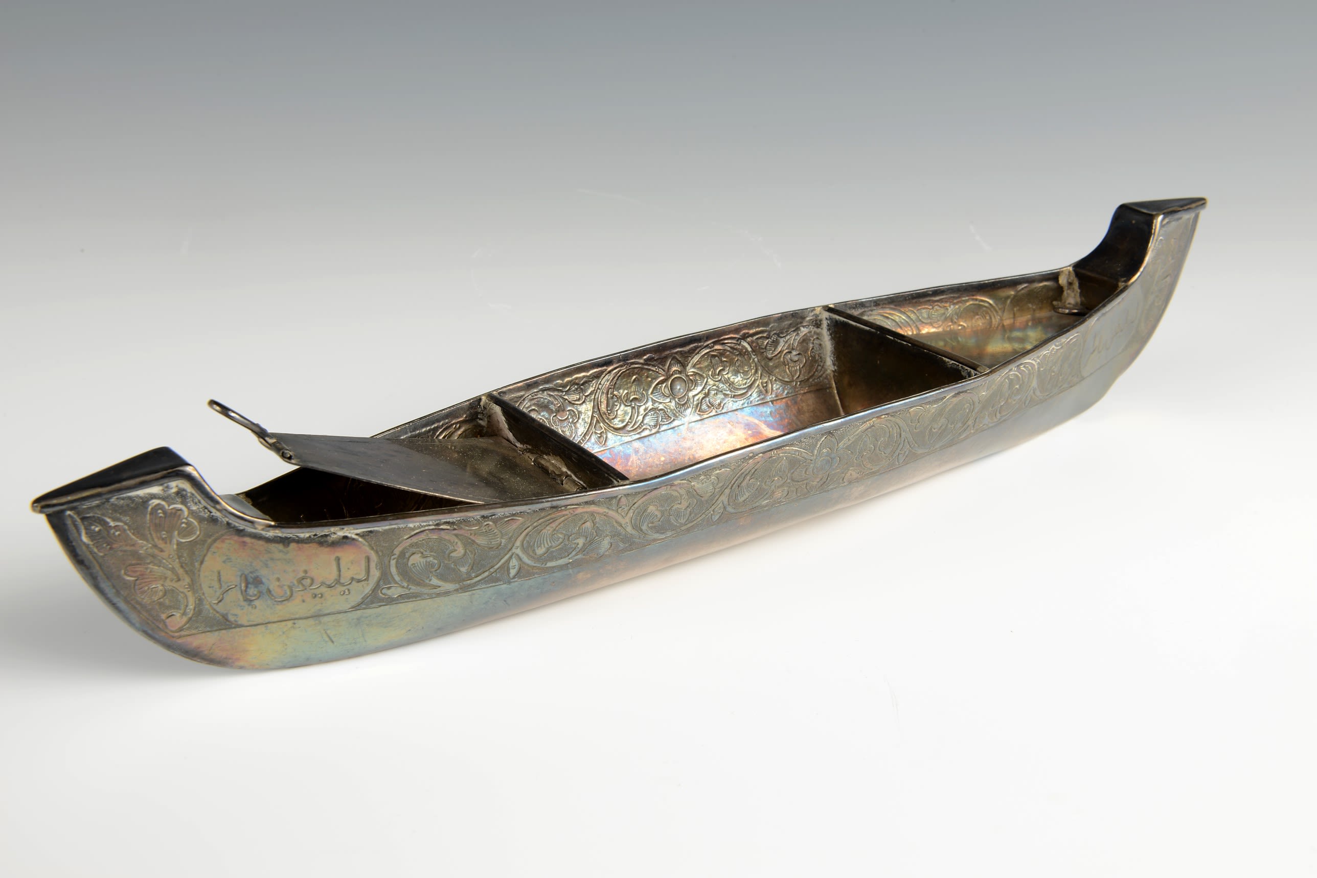 Long, thin canoe shaped ornament in silver metal, with decorative engravings.