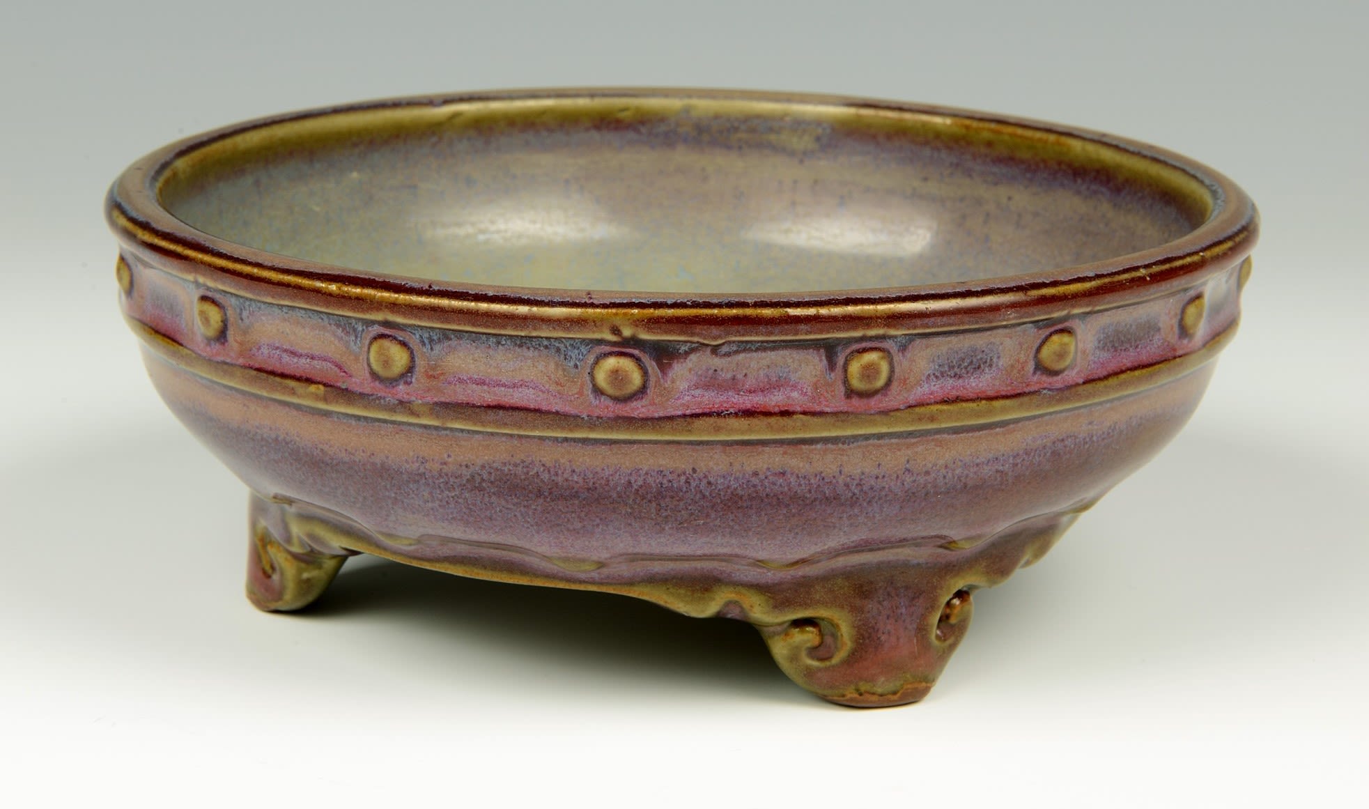 Bowl with a pink, purple and grey glaze. Quite wide in diameter though not tall, with four feet supporting it.