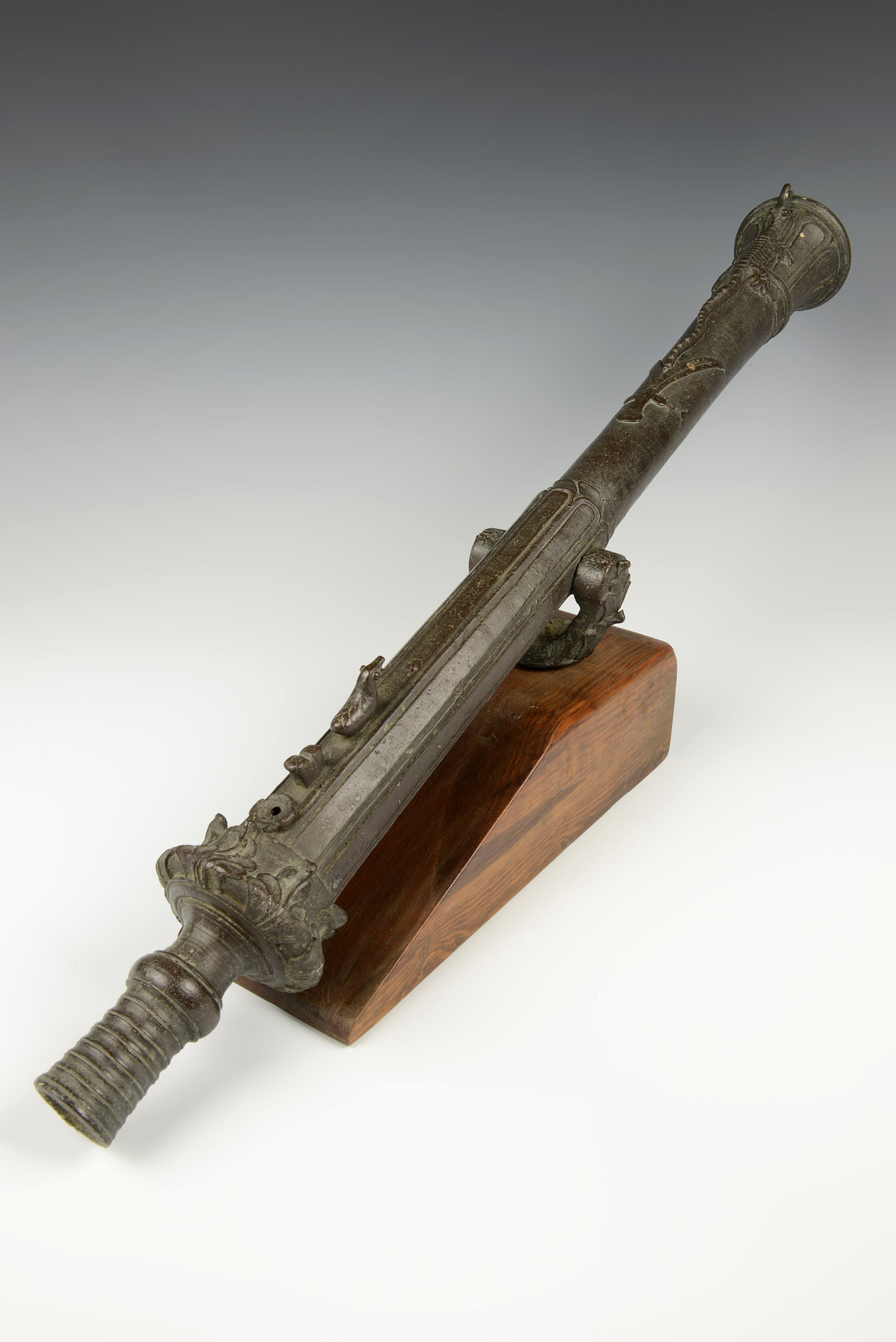Long and thin dark grey cannon, tubular in shape, sat on a brown wooden base.