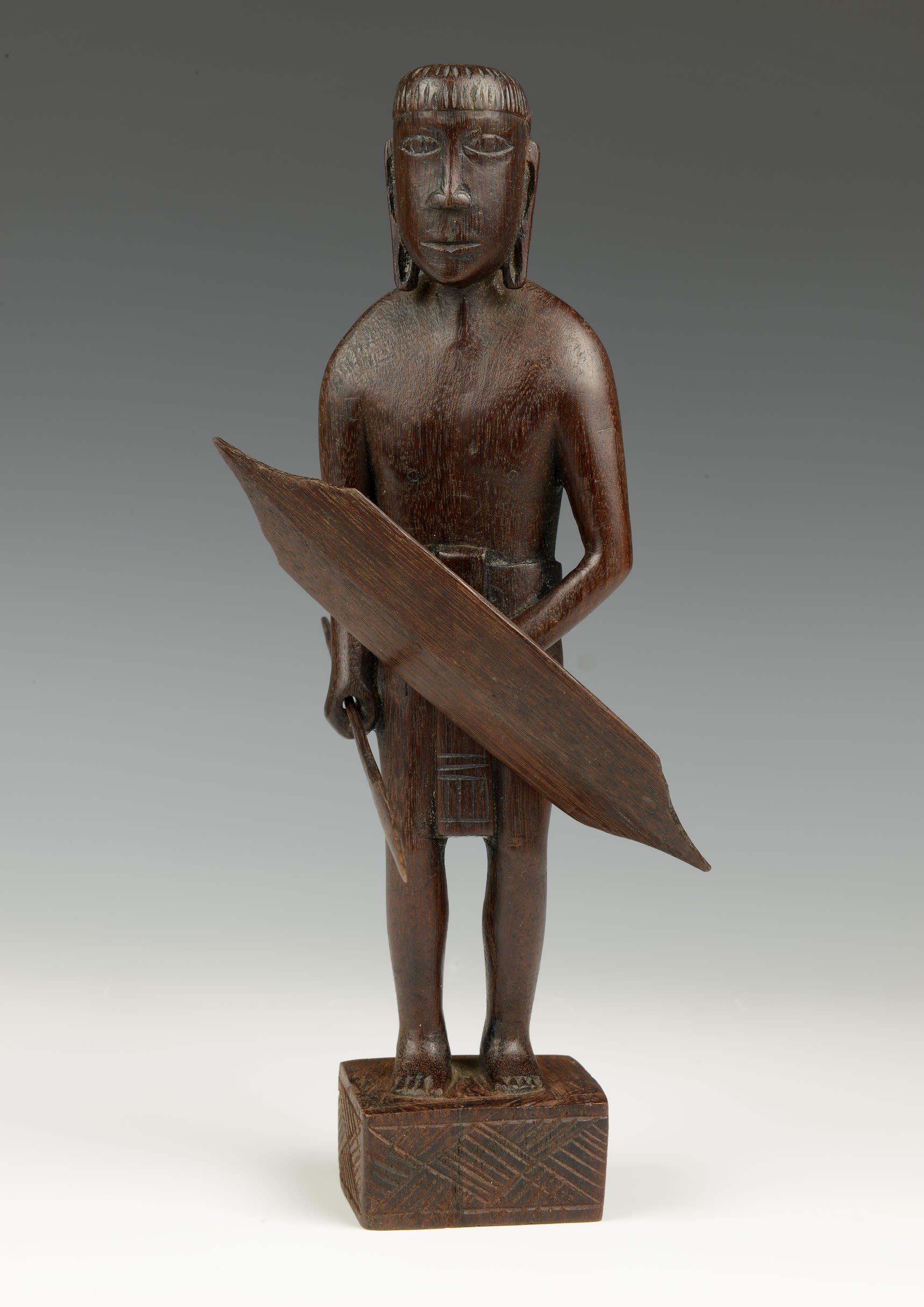 Brown wooden carving of a tall man holding a shield.