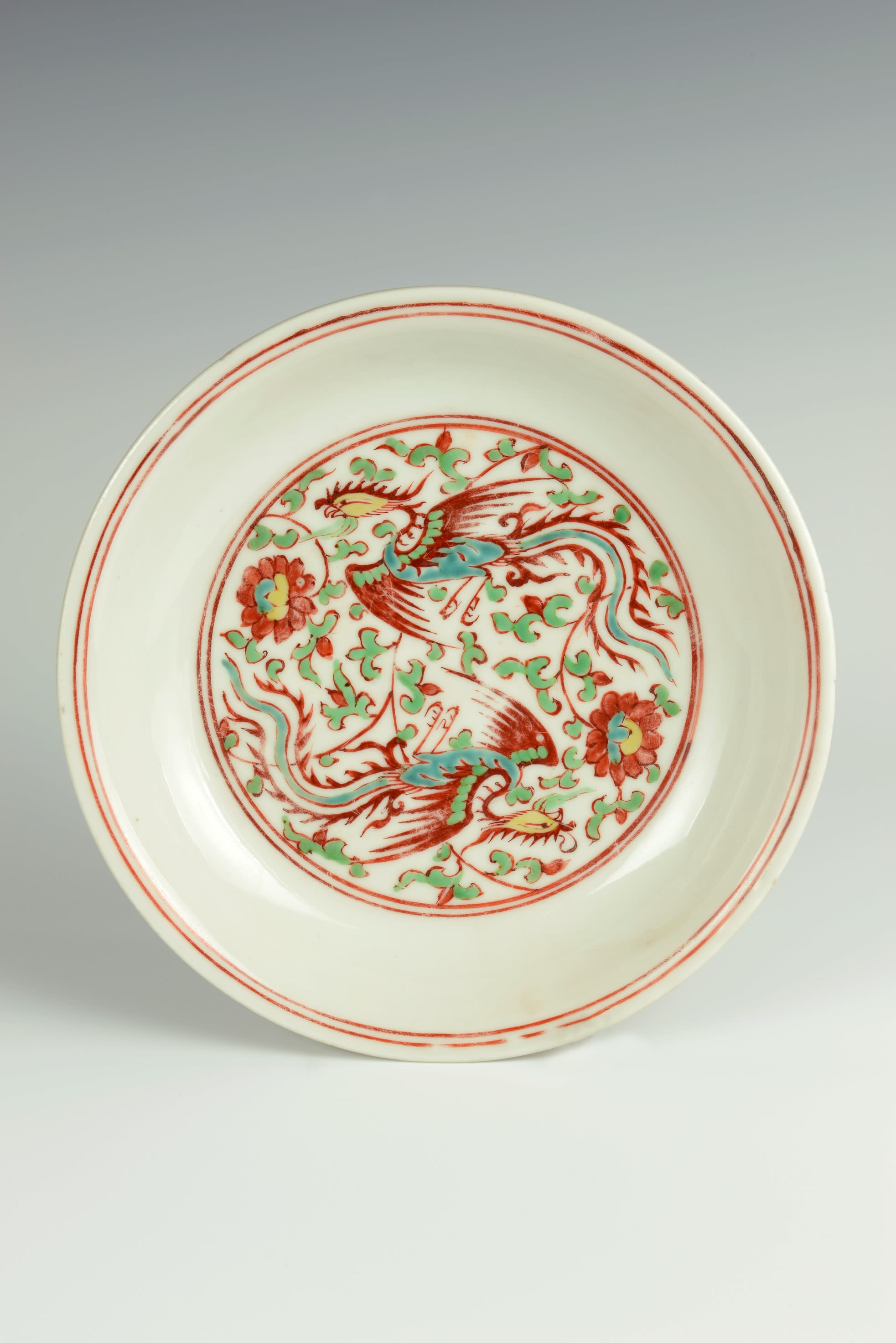 Ceramic plate with a white base, decorated with floral and winged patterns in red, green, yellow and blue.
