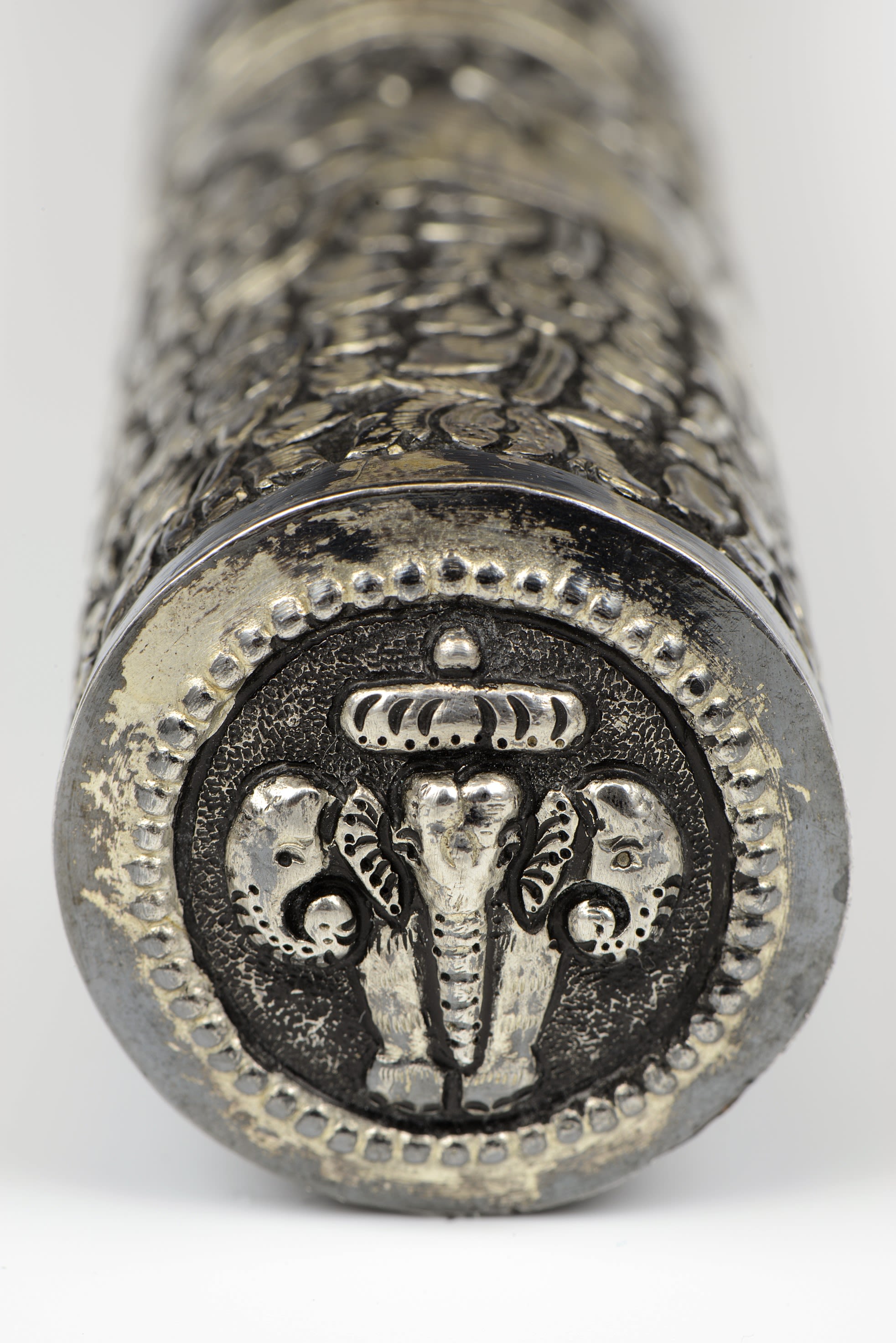 Close up on the circular top of the baton, showing a faded silver design with the outline of an elephant wearing a crown.