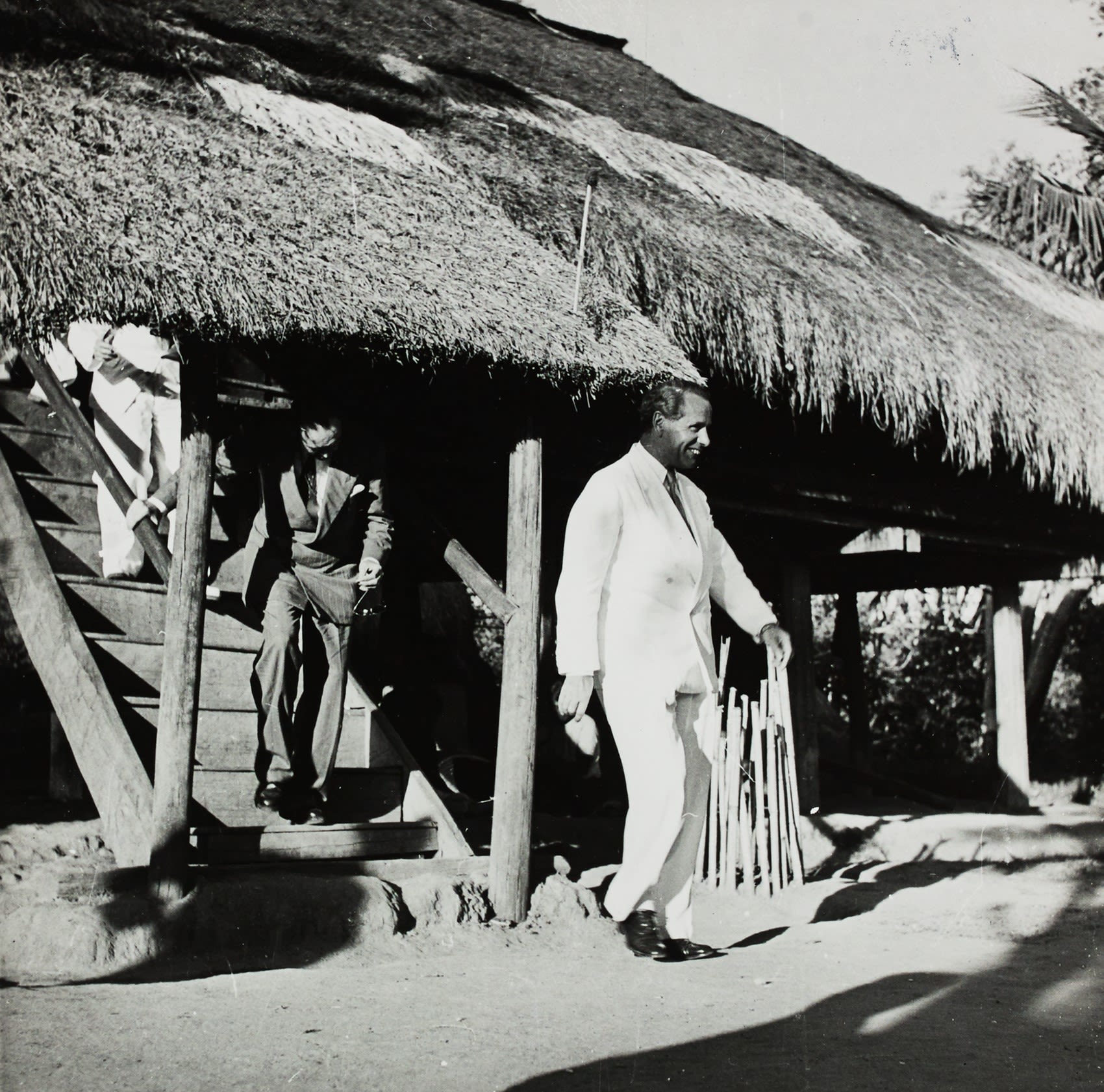 Malcolm MacDonald, dressed in a bright white suit strides forward out of a house