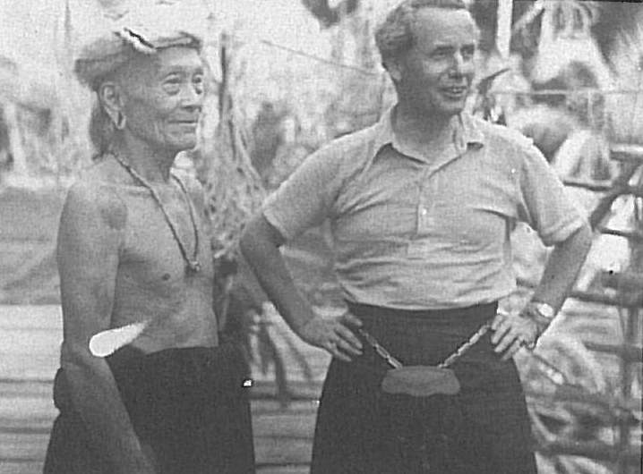 Malcolm stands with hands on hips, wearing a kilt, alongside Temenggong Koh.