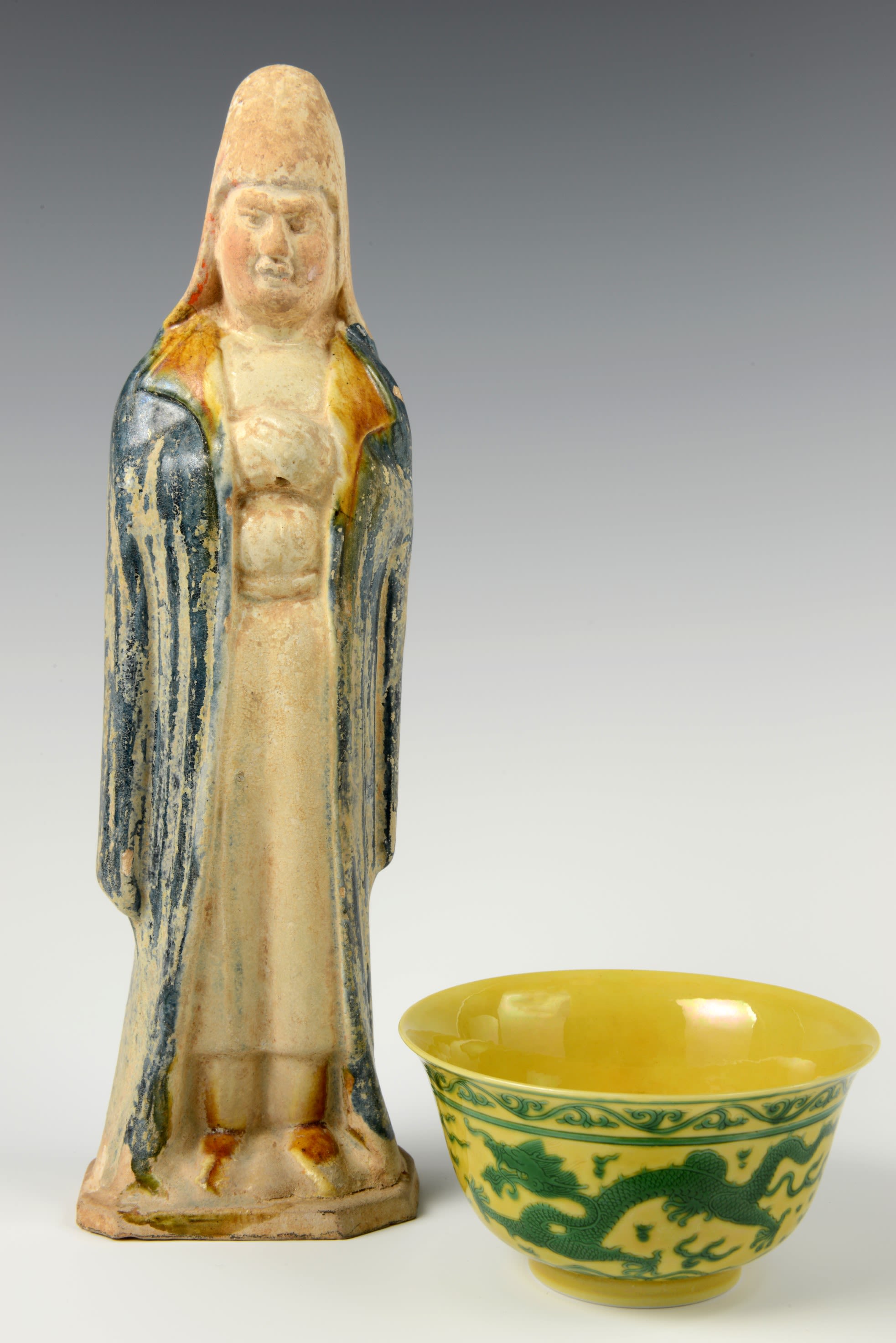 Two objects side by side, a tall man with a cloak and hat and a small yellow and green patterned bowl.