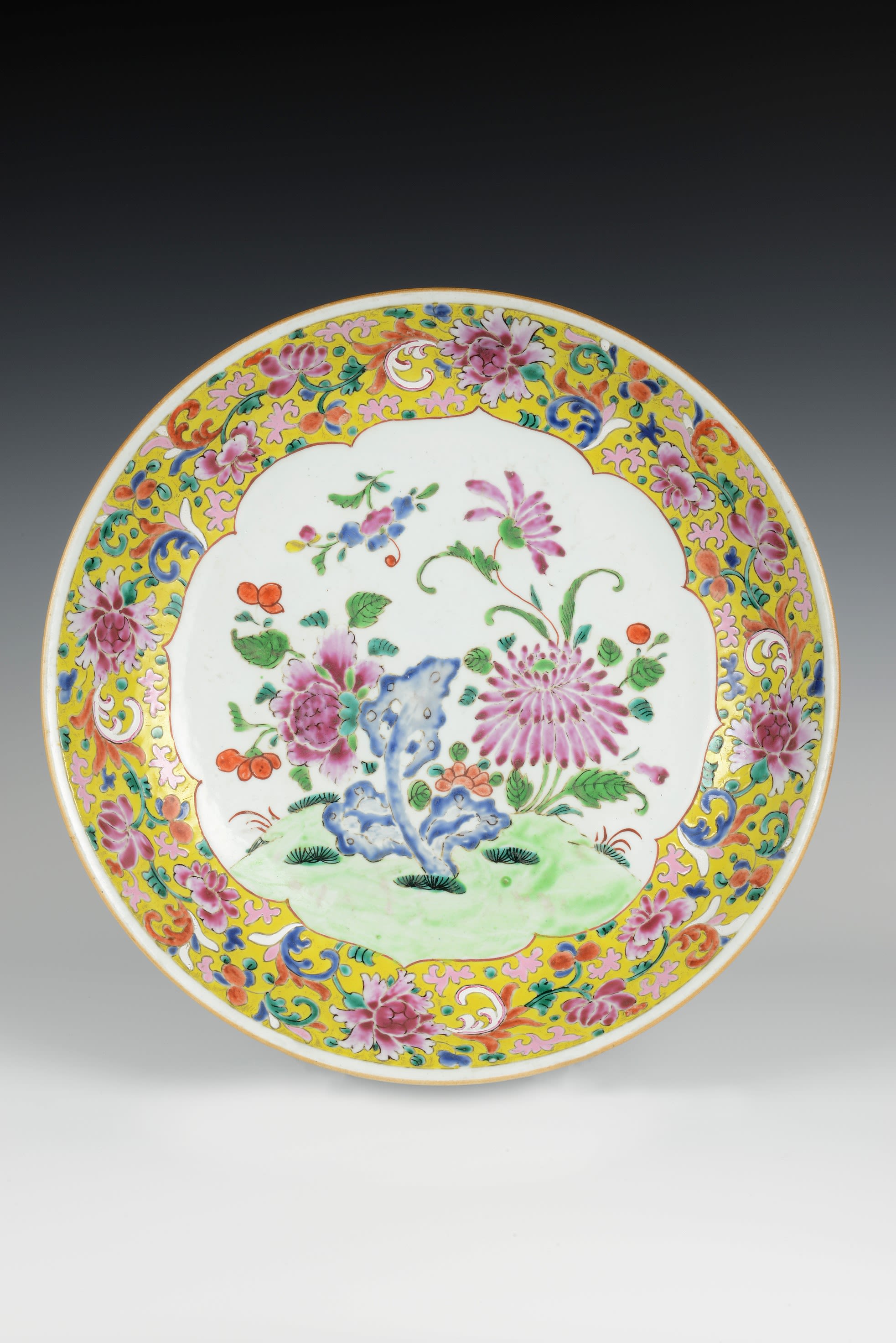 An intricately decorated white plate with a golden trim. The central design is of pink and purple flowers, while the border design includes pink flowers and green foliage.