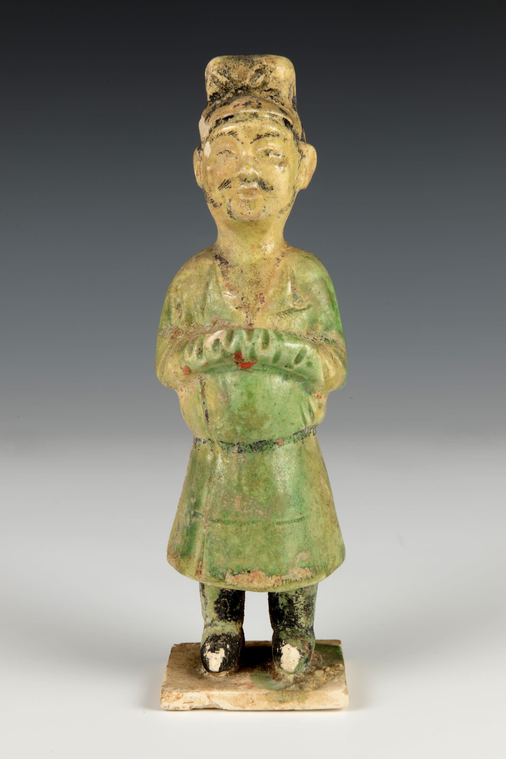 Tall man in a long green and yellow cloak. His arms are clasped together and a faded moustache is visible on his face.
