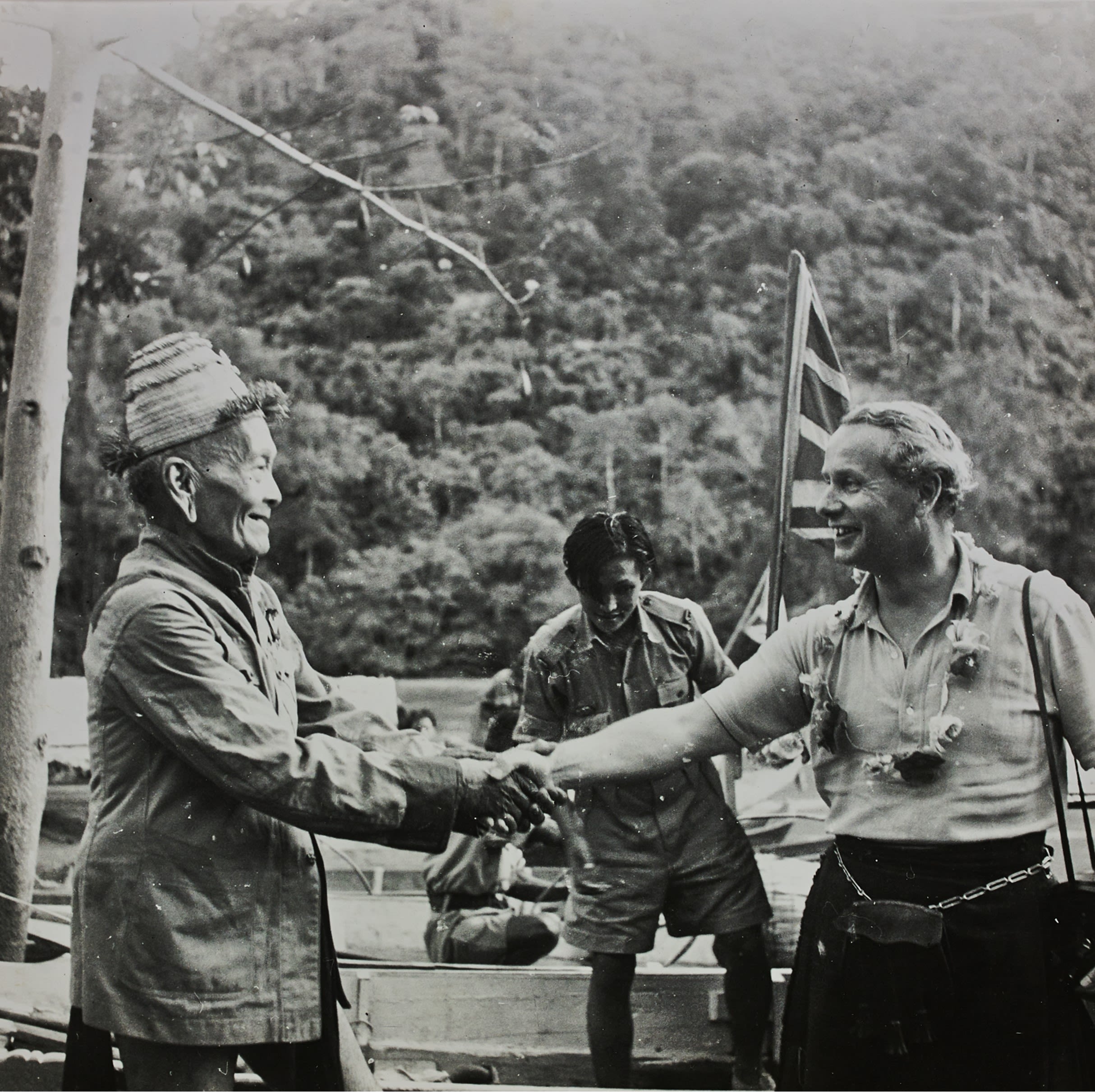 Malcolm MacDonald shaking hands with Borneo head-hunter Temenggong Koh. Both men smile broadly.