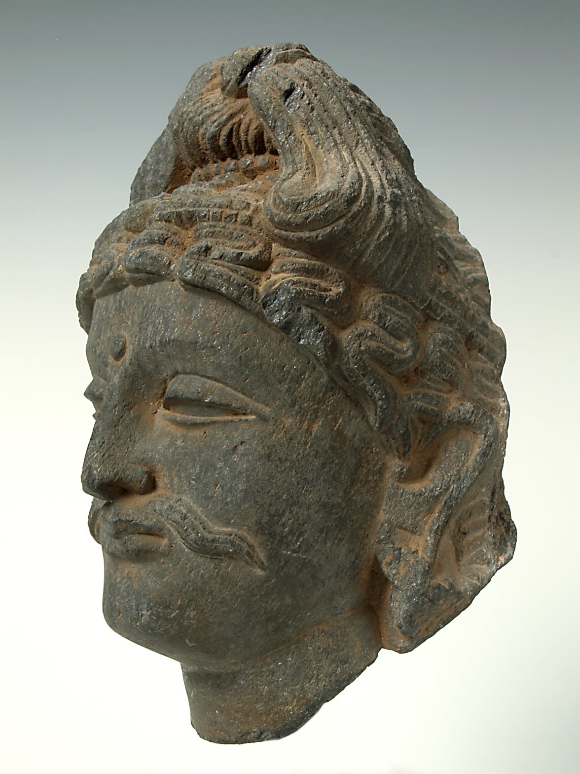 Profile view of a sculpture of a male head and neck, with a prominent wavy moustache.