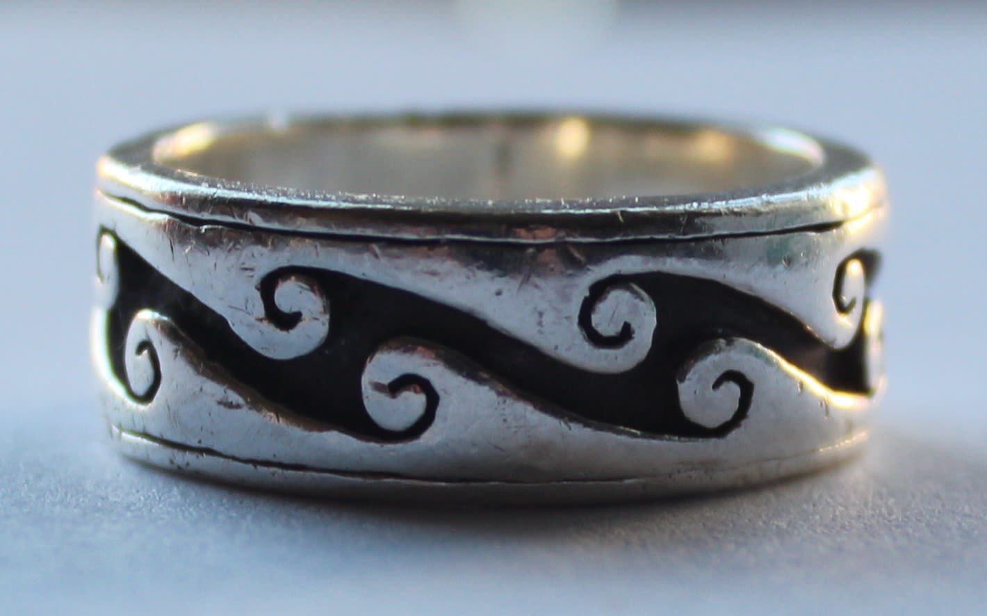 A close-up image of a silver ring with a wave design.