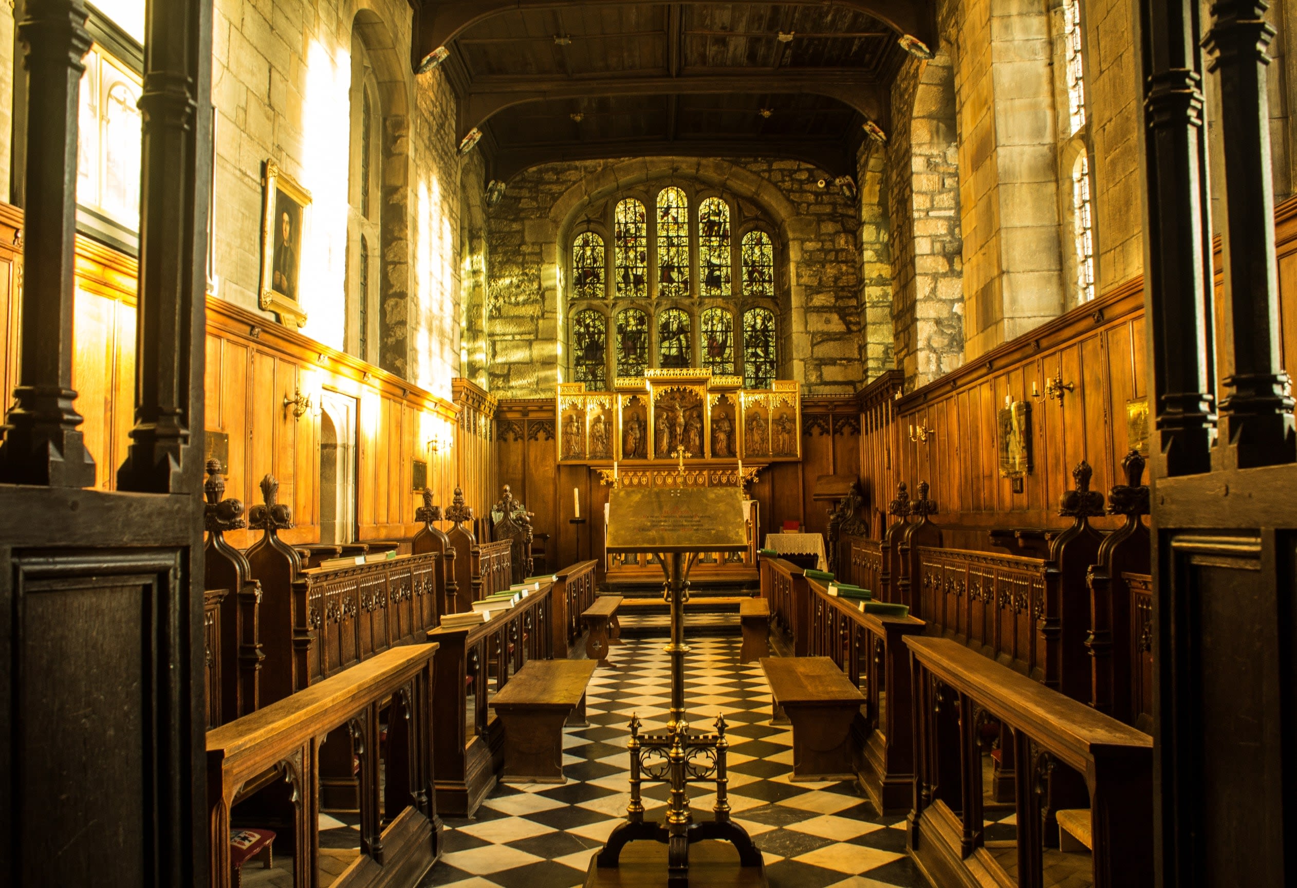 Photo of the interior of the Tunstall Chapel looking towards a golden altar and a large stained glass window showing various religious figures.