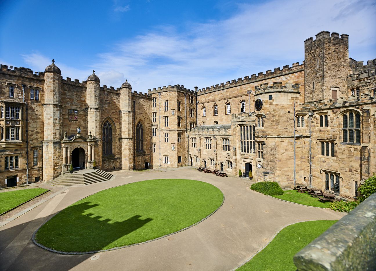 Photo of the courtyard of Durham Castle on a bright day with a blue sky. The stone steps leading to the Great Hall are visible and to the right is the exterior of the Tunstall Gallery and Chapel.