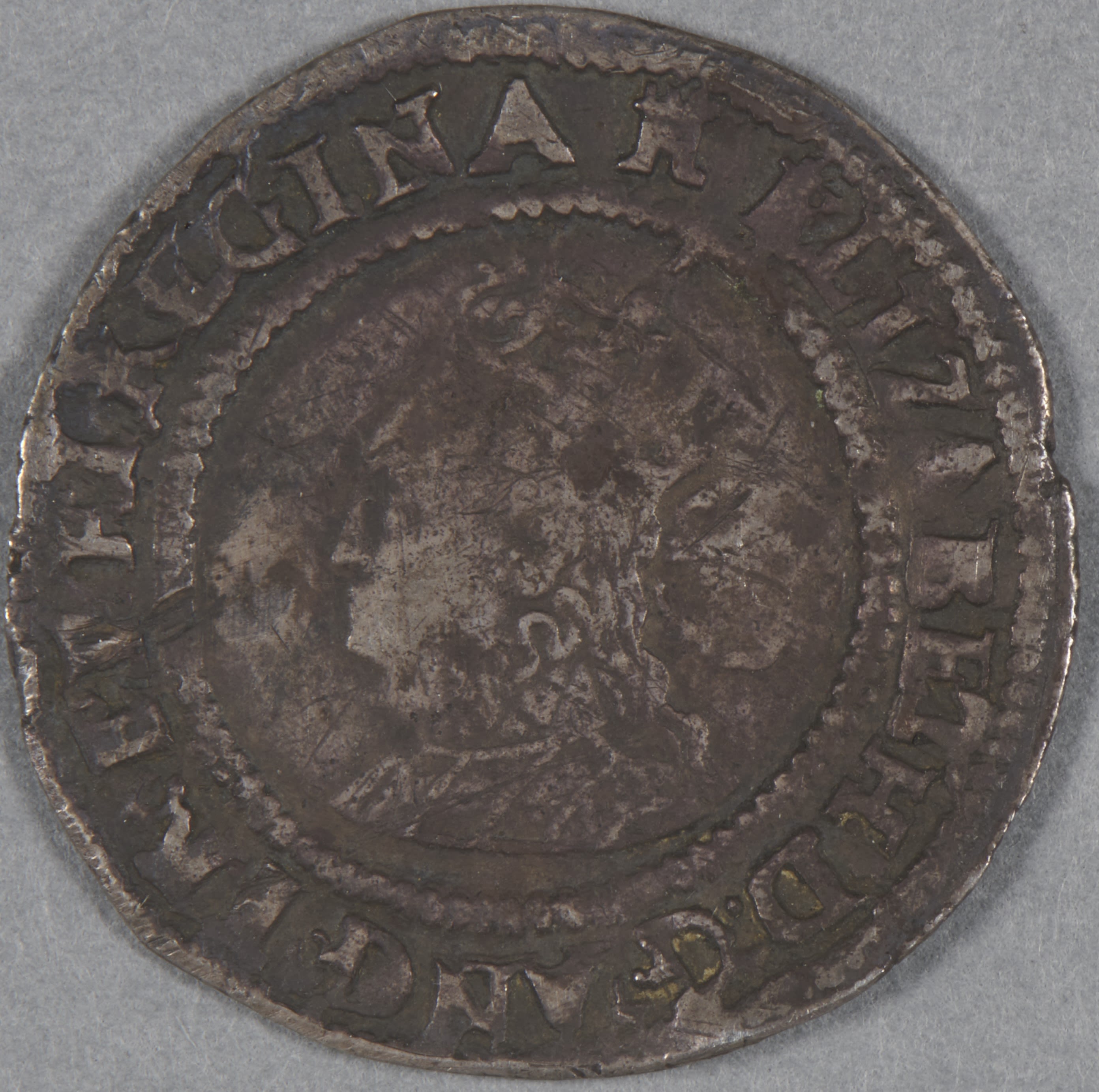 Coin showing a portrait of Elizabeth I. The coin is worn around the edges and has a blackened surface with dirt.