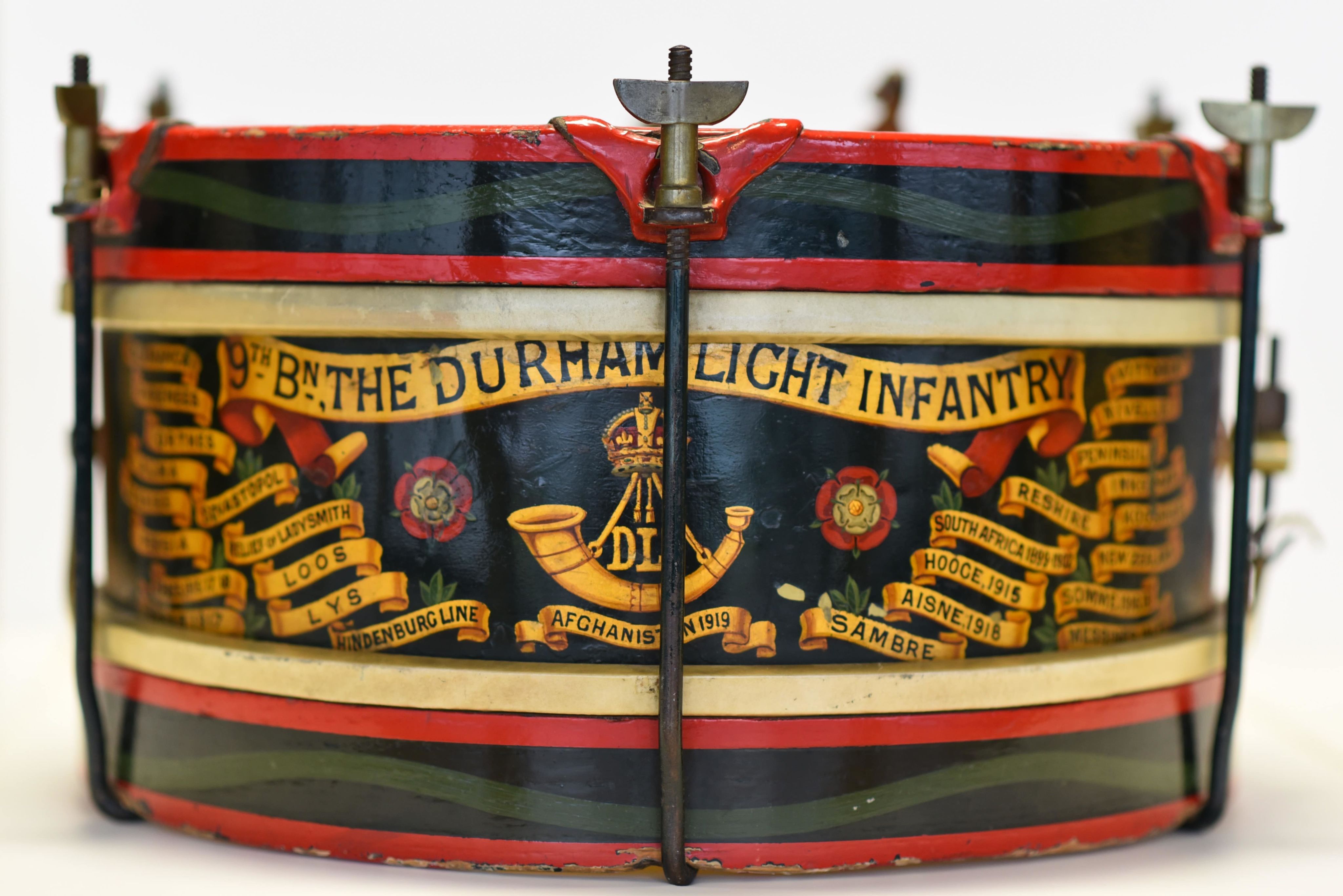 Side view of a blue and red drum with the DLI regimental bugle in the centre and text of many battle honours. Text at top of the drum reads: 9th battalion Durham Light Infantry.