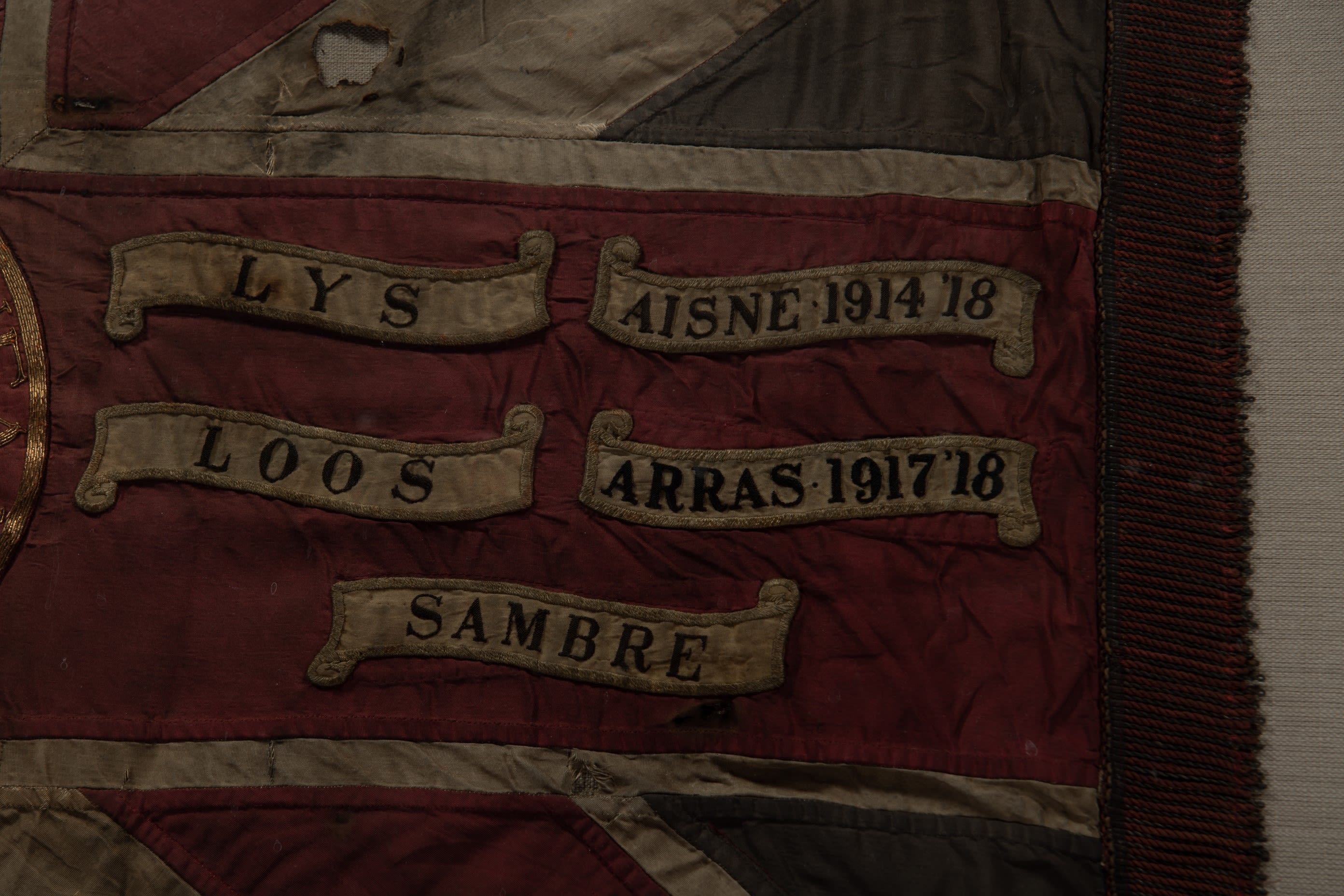 Close up photograph of battle honours on a King's Colour of the DLI. Battle honours include, Lys, Loos, Sambre, Aisne and Arras.